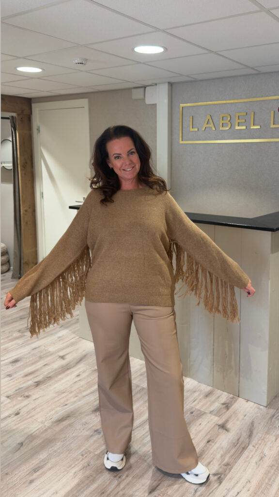 Camel trui met franjes, gecombineerd met een lichte pantalon in onze boutique